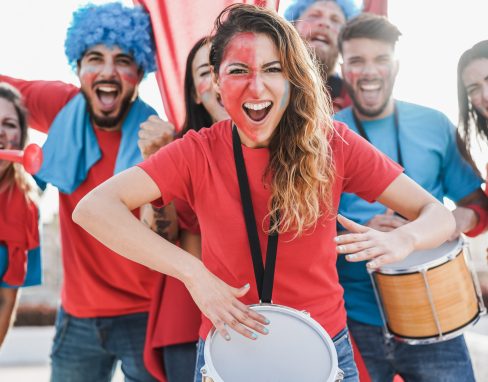 Crazy sport fans playing drums and screaming while supporting their team - Focus on center woman